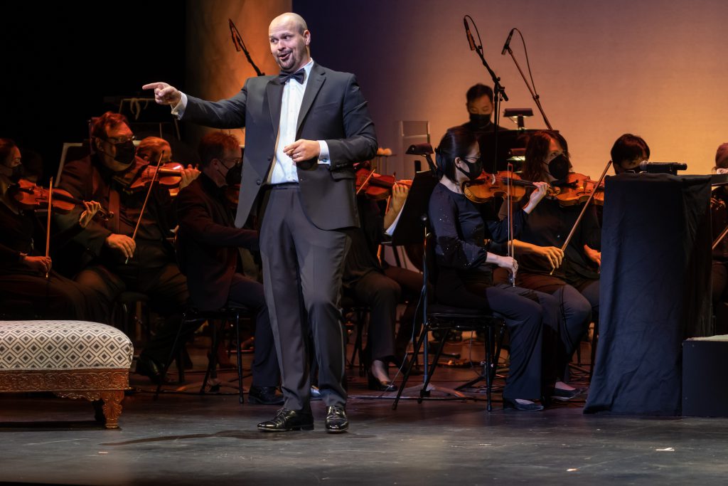 Edward Parks singing, smiling and pointing, with members of the Kansas City Symphony performing behind him. 