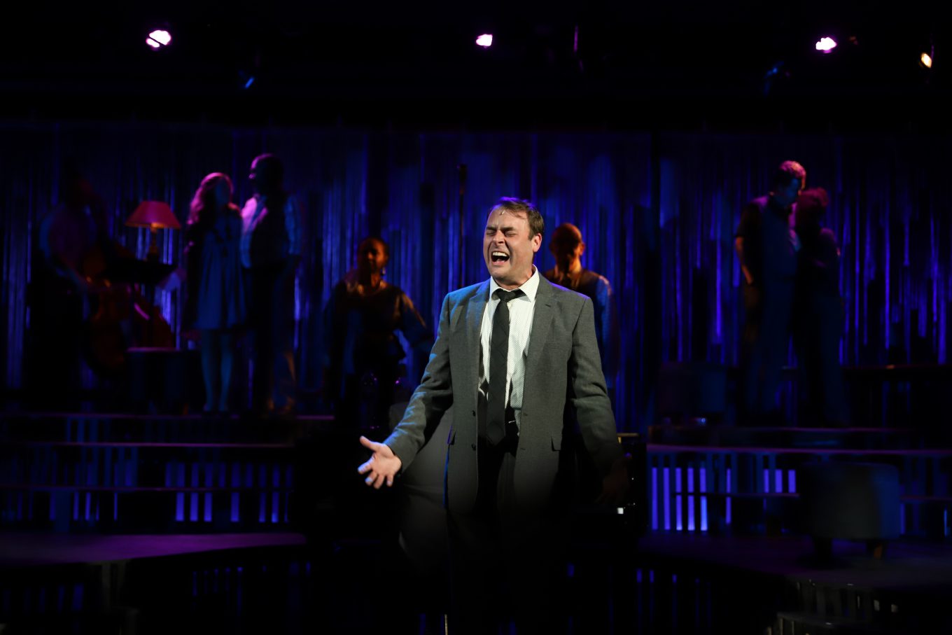 Seth Golay sings on a darkened stage as Bobby in Company.