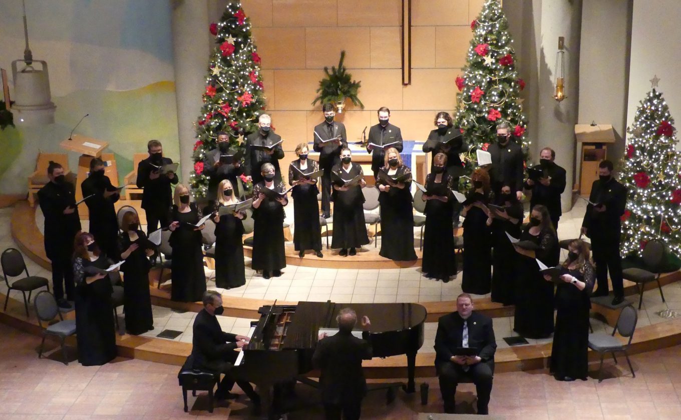 Kansas City Chorale, dressed in black, with Christmas trees behind them.