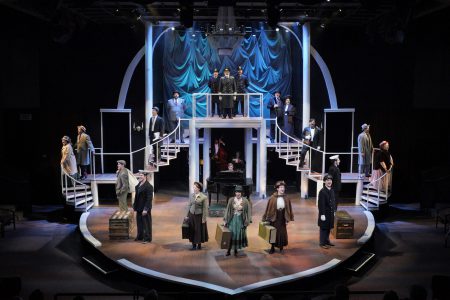 The cast of "Titanic" the musical on stage, in front of a grand staircase.