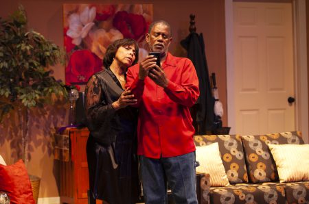 An older Black couple looks at a cell phone with puzzled expressions.