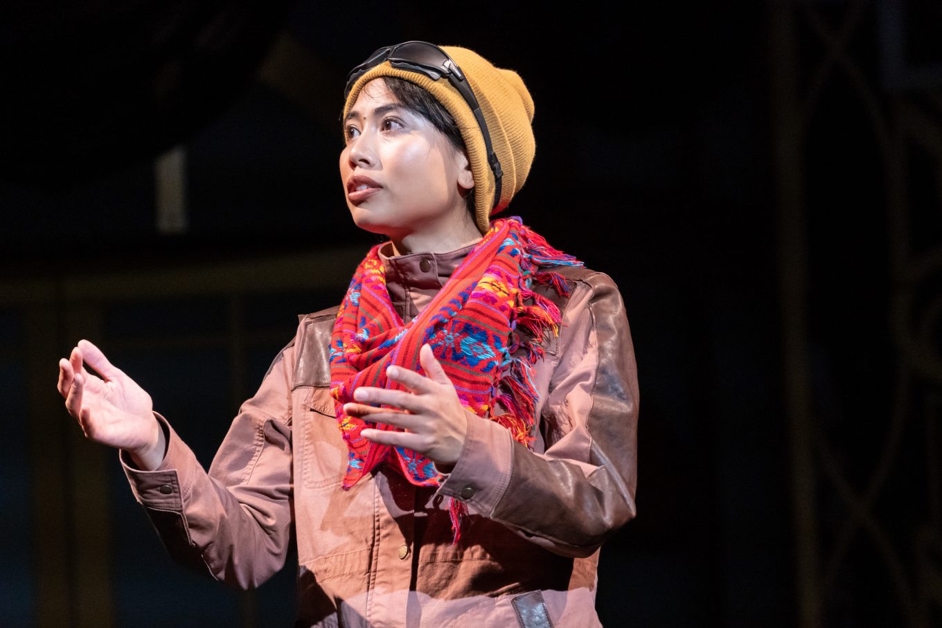 A young woman dressed in a disguise of a knit cap, scarf and coat, talks and gestures