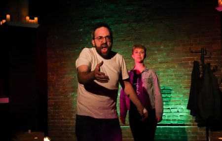 Faustus speaks passionately while a oung woman (Mephistopheles) stands behind him, smiling