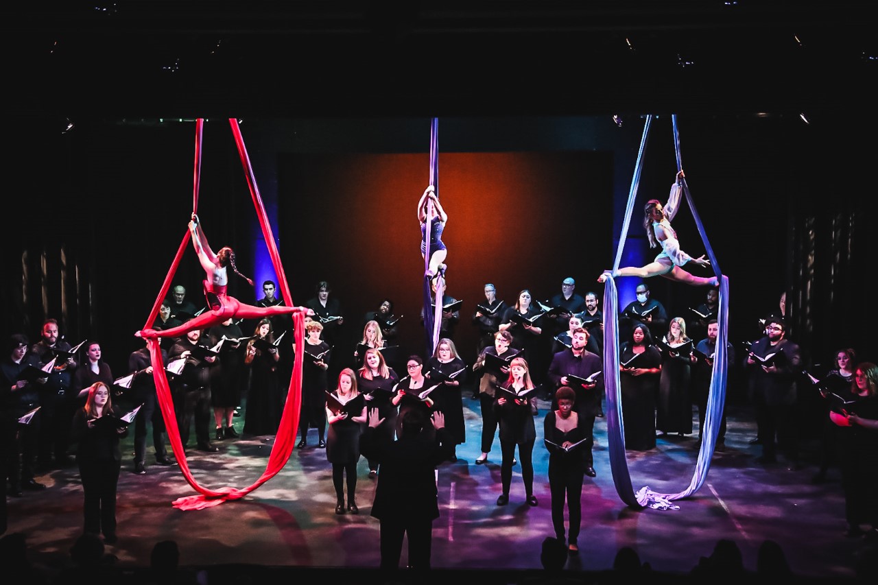 Aerialists perform on silks above a choir .
