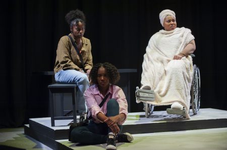 Three Black women sit together looking forlorn in a scene from Is God Is.