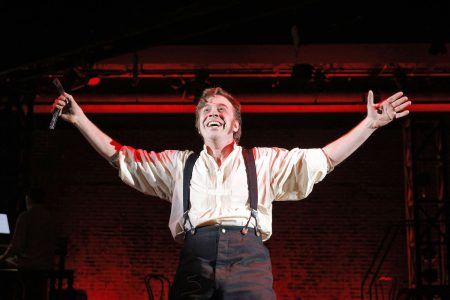 A man cast in red light holds his arms out and gives an evil grin.