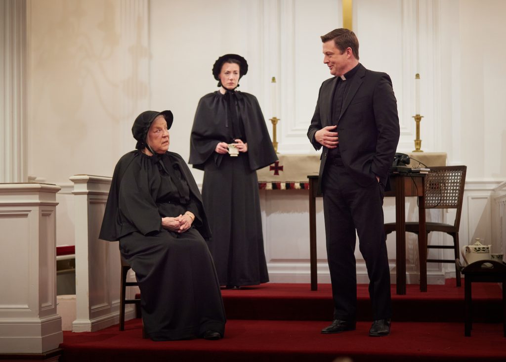 Actors playing a Catholic priest and two nuns perform a scene inside a church.