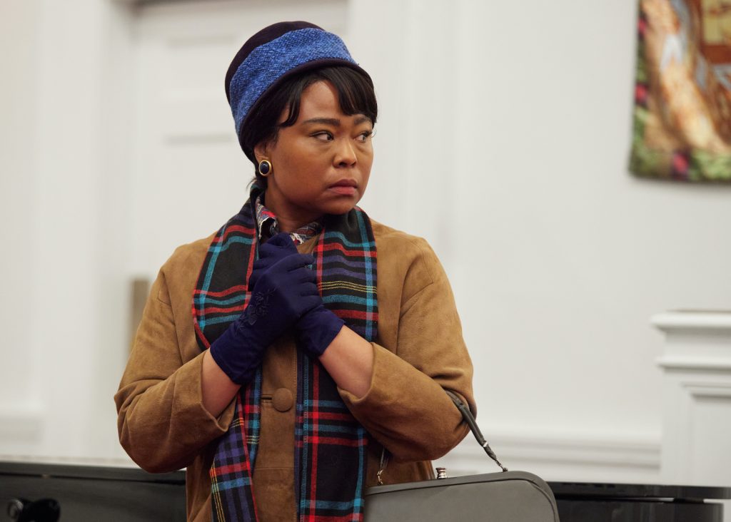 A young Black woman dressed in 1960s clothing looks worried.