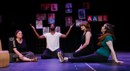 Three white actresses sit on the floor around their Black director, kneeling with his arms outstretched.