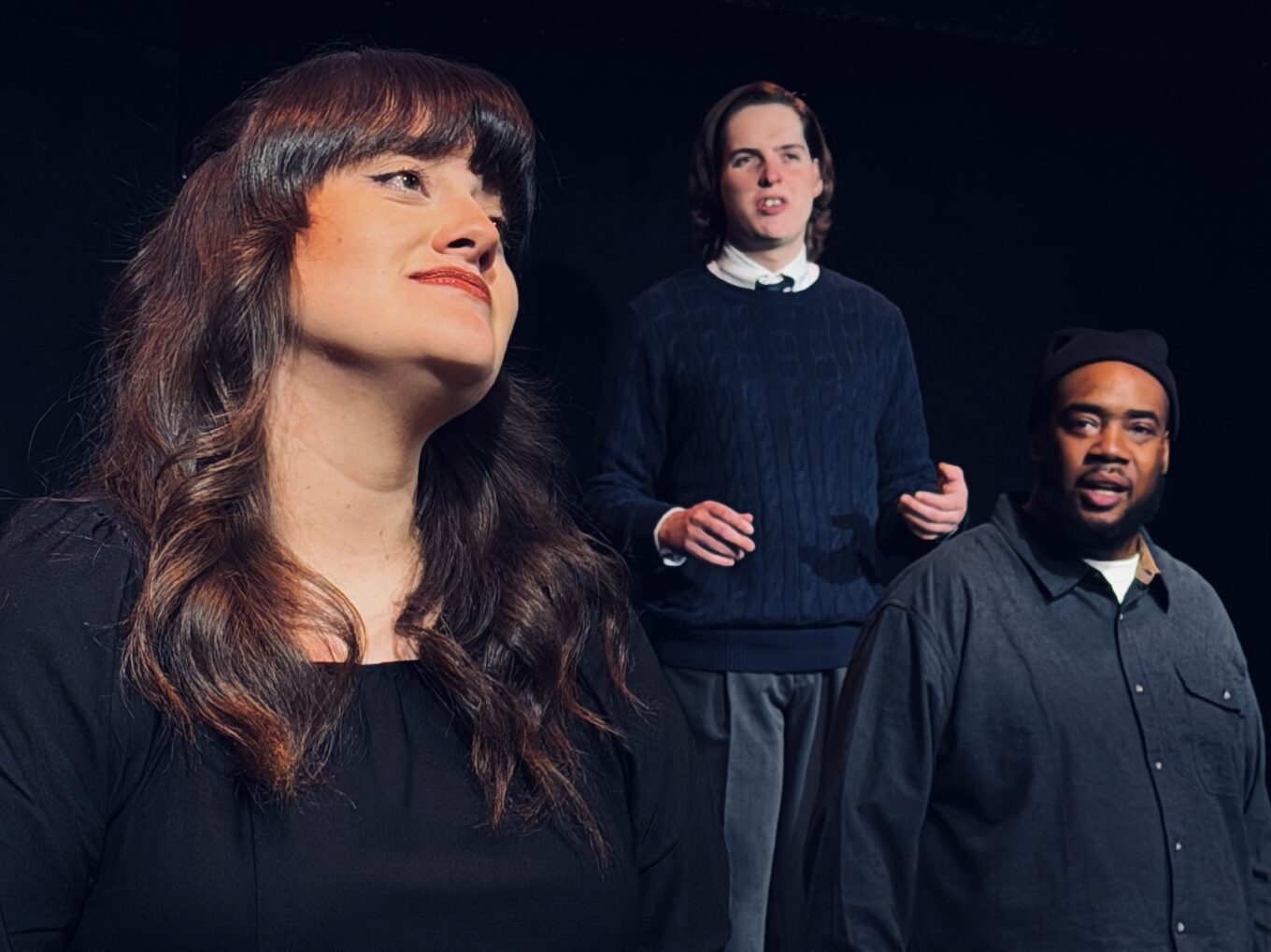 A close-up on a young woman's face, looking off, Two actors are behind her, looking at her with looks of disbelief or disapproval.